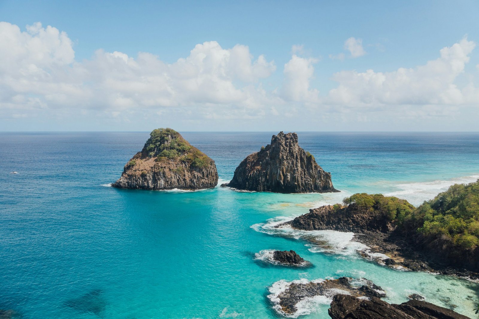 brown and green rock formation on blue sea under white clouds and blue sky during daytime